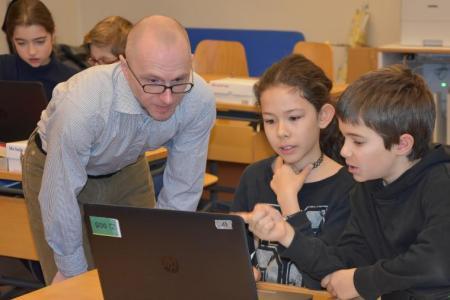 Eine Lehrperson unterstützt eine Schülerin und einen Schüler bei der Arbeit am Computer.
