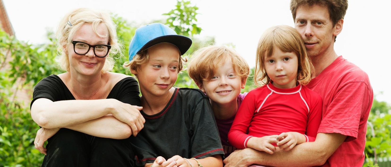 Eine Familie mit drei Kindern sitzt im Garten auf einer Holzpalette und lacht in die Kamera.