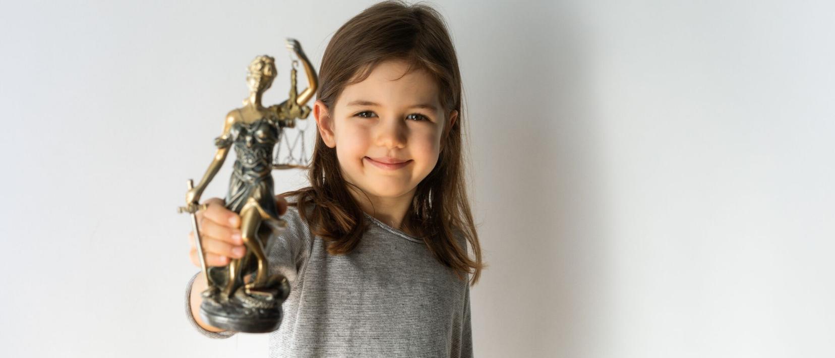Ein Mädchen hält eine Figur der Justizia hoch und lächelt