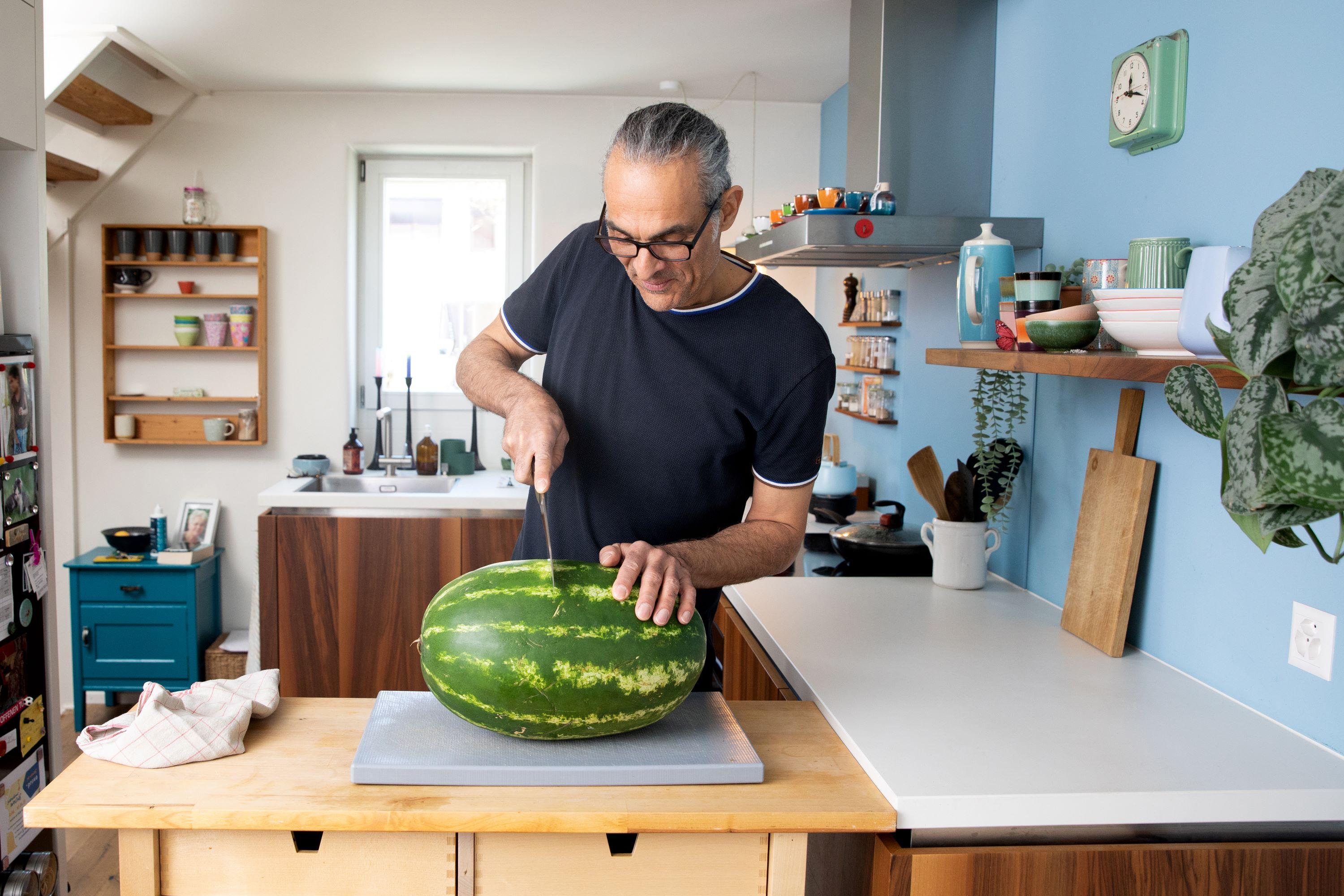 Mitarbeiter in der Freizeit in der Küche am Schneiden einer Wassermelone auf einem Schneidbrett.