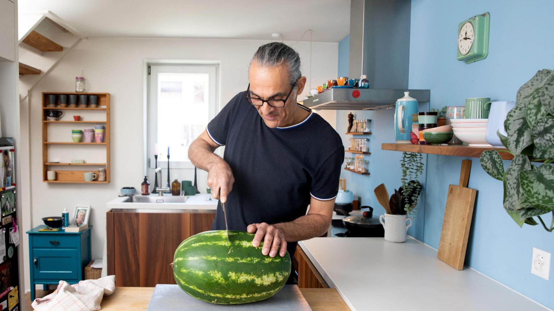 Mitarbeiter in der Freizeit in der Küche am Schneiden einer Wassermelone auf einem Schneidbrett.