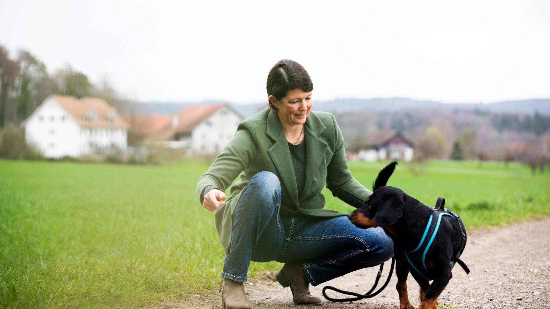 Mitarbeiterin in der Freizeit kniet auf einem Feldweg und spielt mit ihrem Hund.