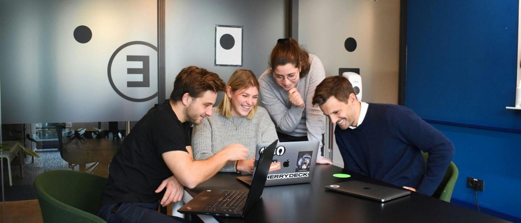Vier Personen sitzen an einem Besprechungstisch und schauen gemeinsam in einen Laptop.
