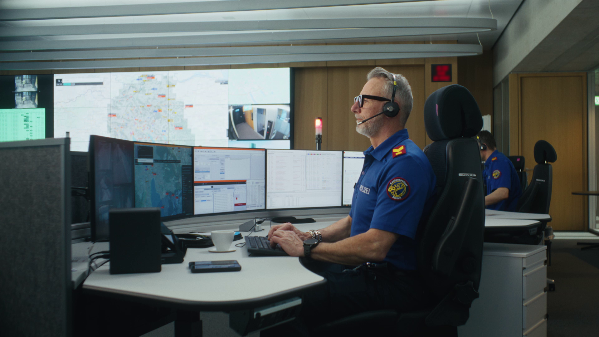 Polizist sitzend am Schreibtisch vor dem Computer in der Einsatzzentrale.