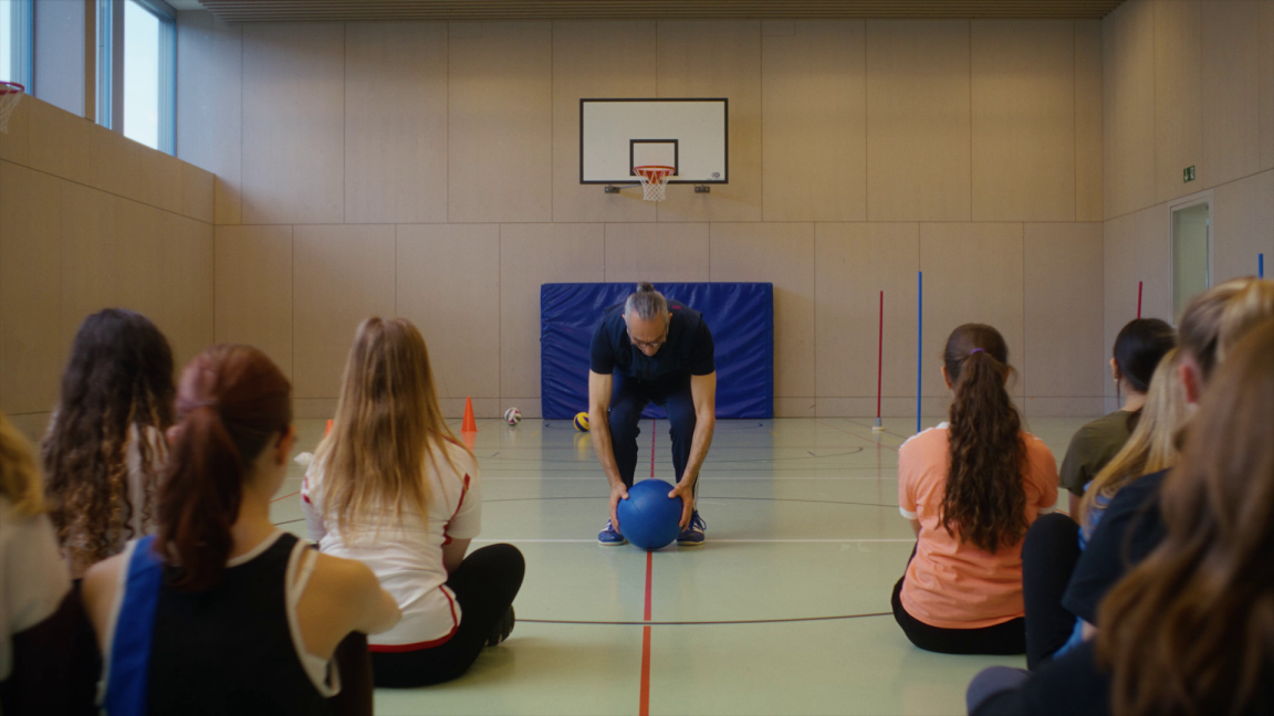  Ein Sportlehrer macht Übungen in einer Turnhalle vor