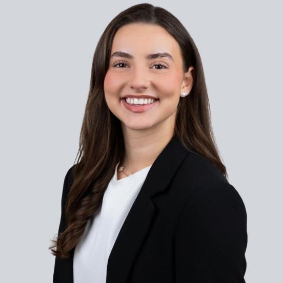 Ein Portraitbild, das unsere Lernende mit langen dunkelbraunen Haaren und einem schwarzen Blaser zeigt.