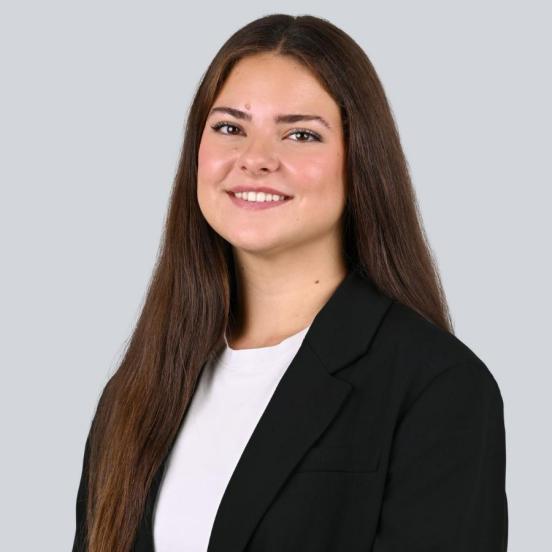 Ein Portraitbild, das unsere Lernende mit langen braunen Haaren und einem dunklen Blazer zeigt.