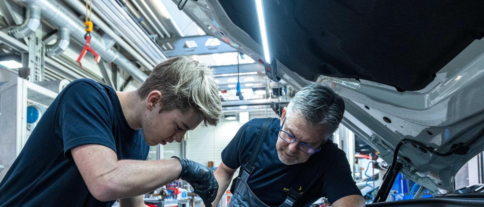 Ein Lehrling und sein Lehrmeister arbeiten an einem Motor eines Fahrzeuges