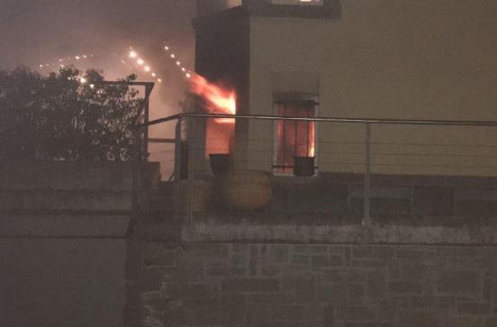 Hausfassade mit Flammen die aus einem Fenster schlagen