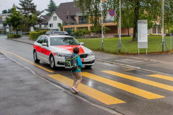SChulkind läuft vor Polizeifahrzeug über den Fussgängerstreifen 