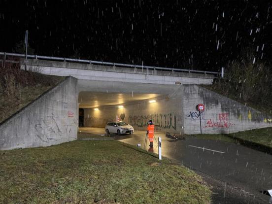 Polizist beim Fotografieren vor einem Unfallauto unter einer Autobahnbrücke