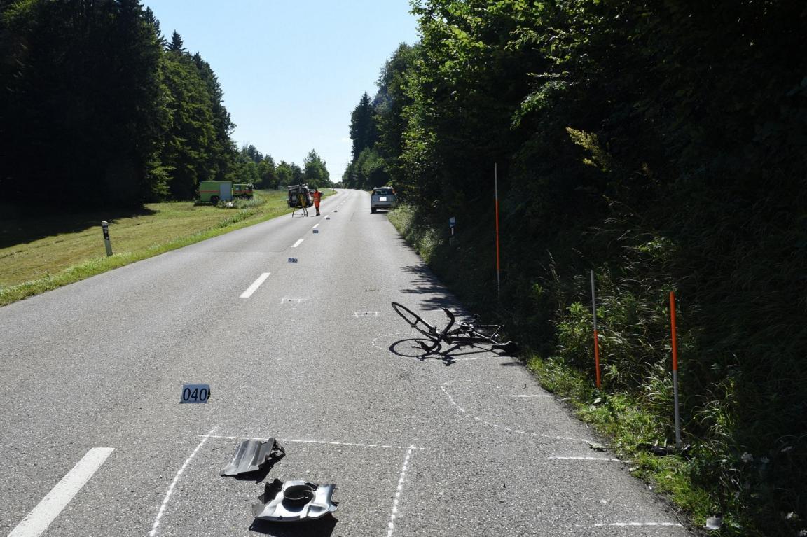Überlandstrasse in Waldbereich mit am Boden liegendem Fahrrad sowie Polizei bei der Unfallaufnahme
