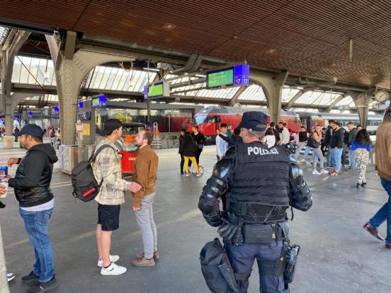 Polizist steht in der Halle des Hauptbahnhofs. Im Hintergrund mehrere Passanten