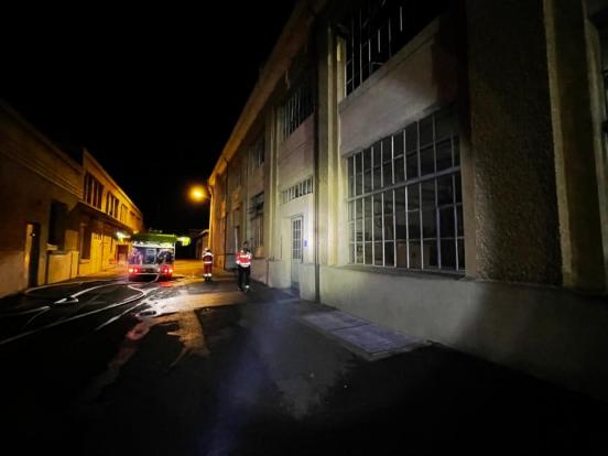 Feuerwehrfahrzeug und ein Polizist zwischen zwei Gewerbegebäuden bei Nacht