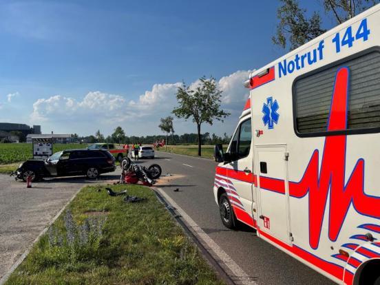 Rettungswagen auf Unfallstelle. Im Hintergrund ein stark beschädigtes Motorrad und ein beschädigter Personenwagen