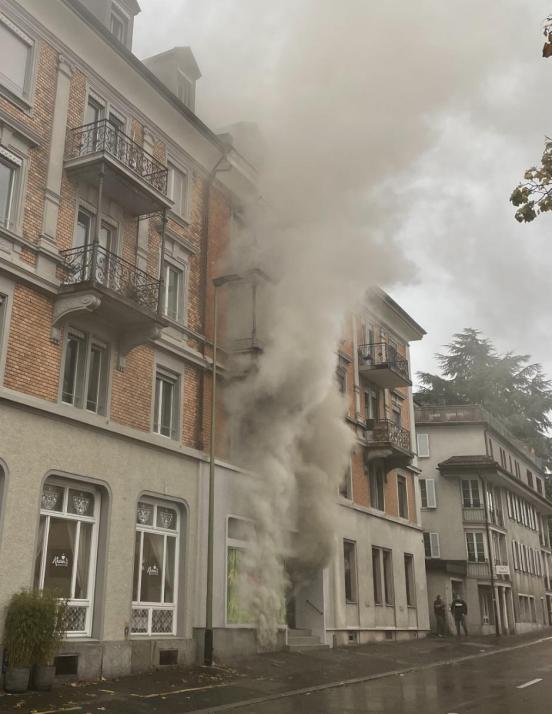 Rauch dringt aus Kellerfenster eines Wohn- und Geschäftshauses