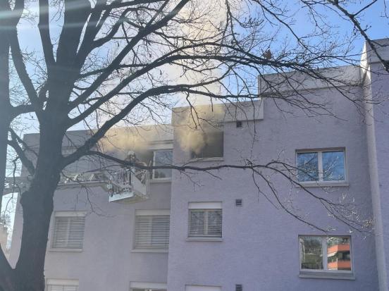 Rauch dringt aus Fenster eines Mehrfamilienhaus, Feuerwehr bei Löscharbeiten