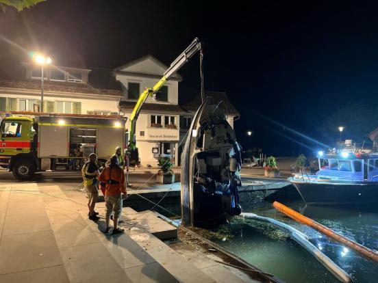 Ein Feuerwehrauto mit Kran zieht ein beschädigtes Motorboot aus dem Wasser