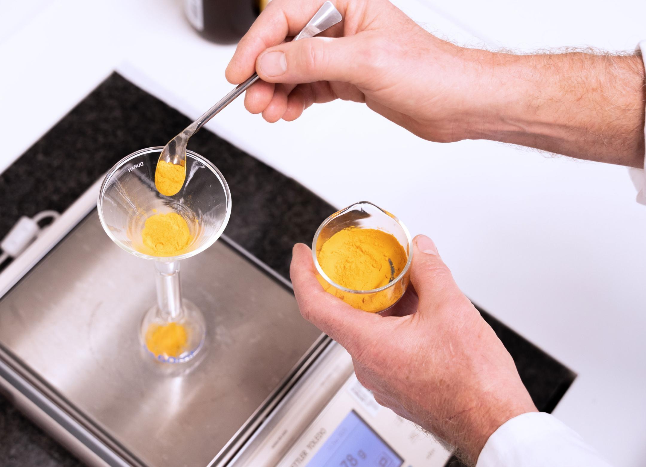 Eine Waage und ein Laborant, der Kurkuma-Gewürzpulver abwägt. 