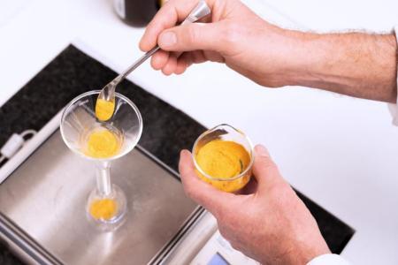 Eine Waage und ein Laborant, der Kurkuma-Gewürzpulver abwägt. 