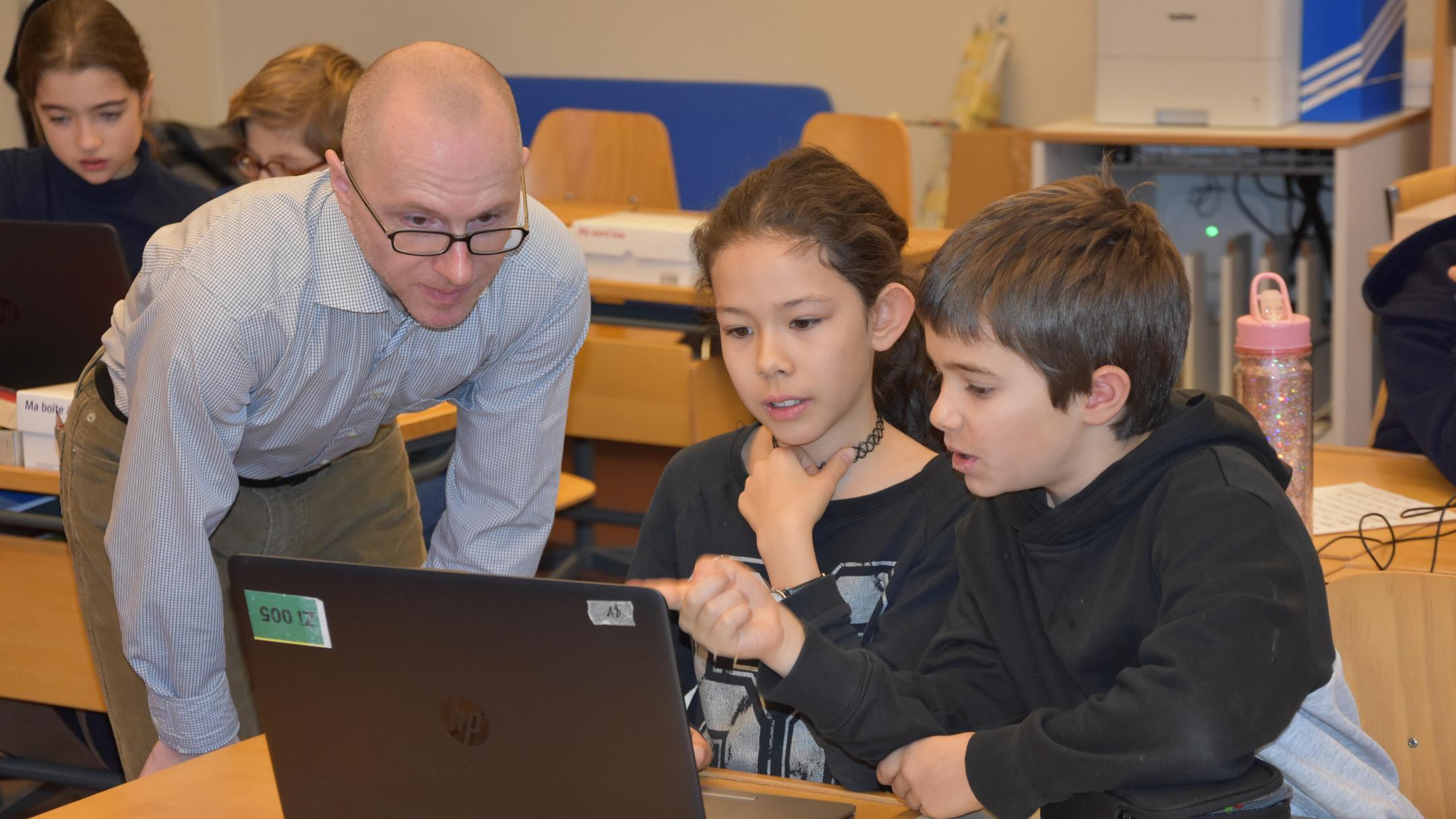 Eine Lehrperson unterstützt eine Schülerin und einen Schüler bei der Arbeit am Computer.