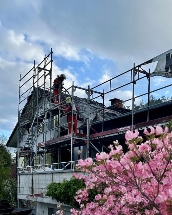 Feuerwehrleute auf einem Baugerüst löschen ein brennendes Haus