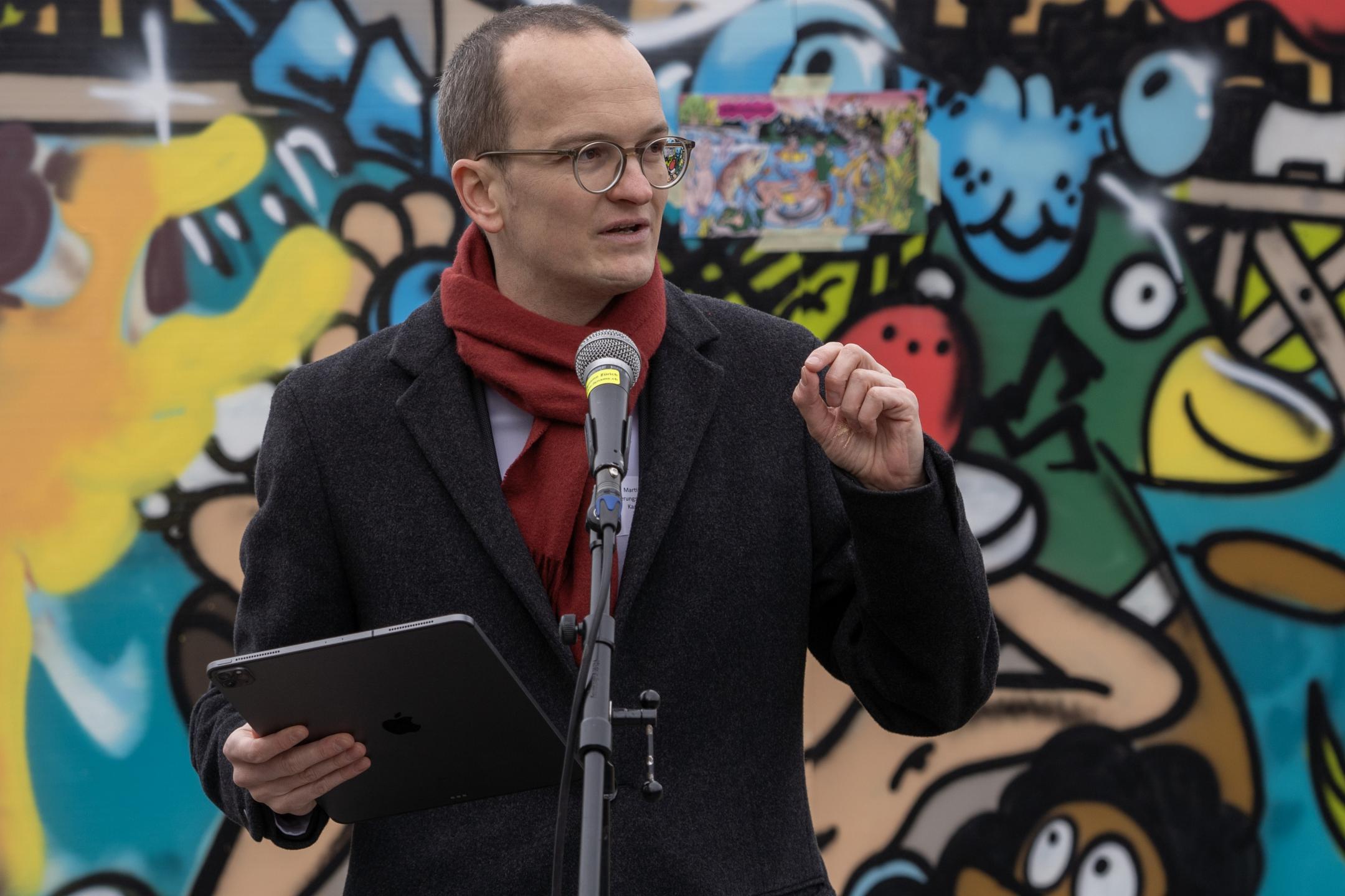 Martin Neukom hält eine Rede. Im Hintergrund ein buntes Graffito.