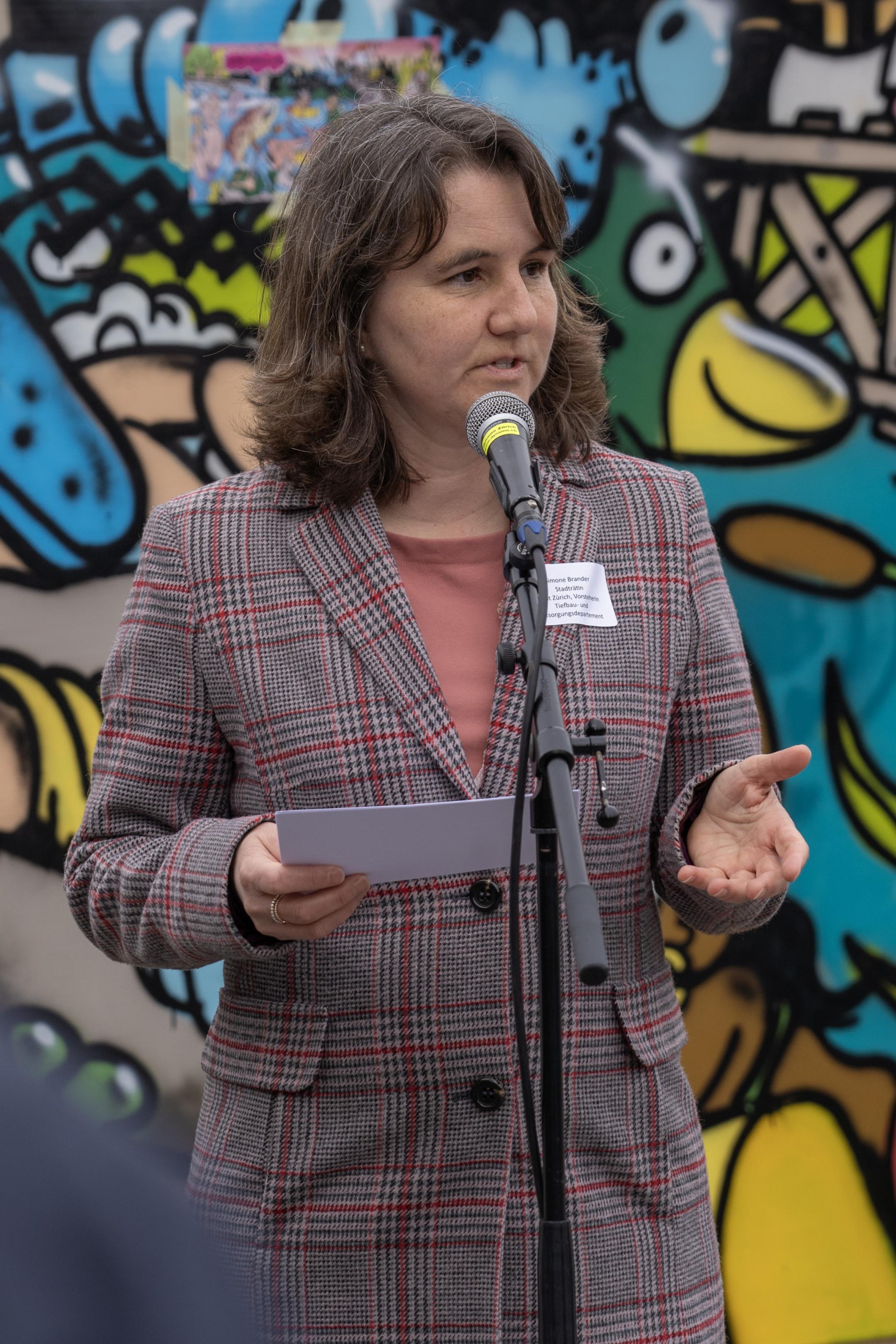 Simone Brander hält eine Rede. Im Hintergrund ein buntes Graffito.