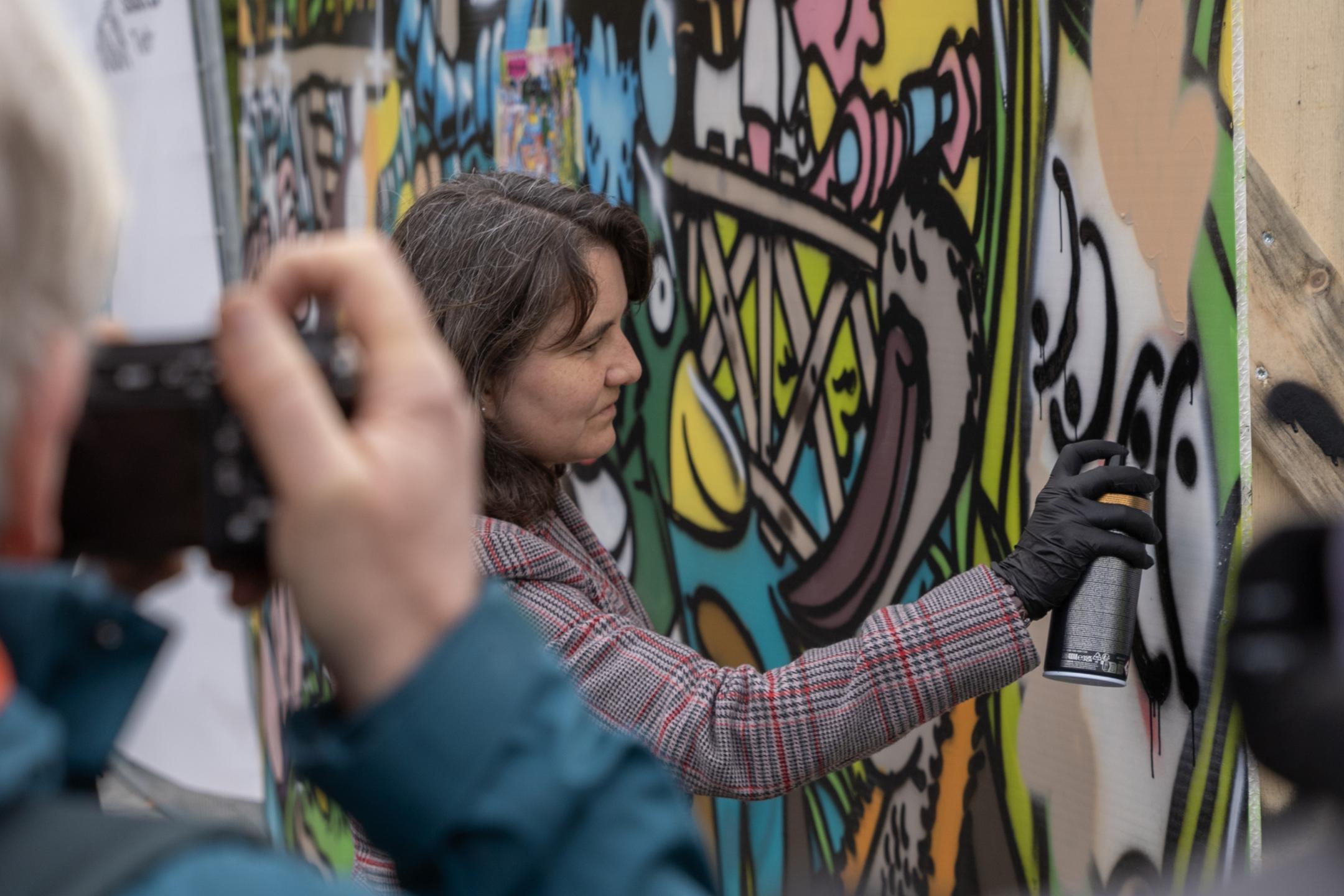 Stadträtin Simone Brander sprüht mit einer Spraydose auf ein Graffito.