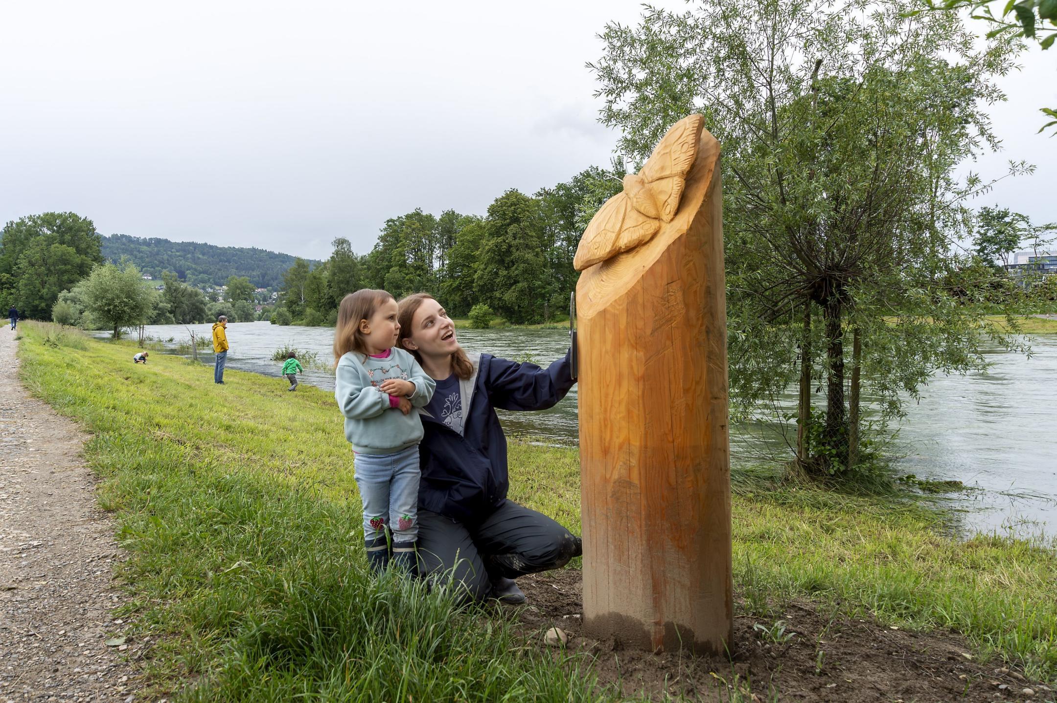 Eine Frau mit einem Kind bewundert eine geschnitzte Schmetterlingsfigur