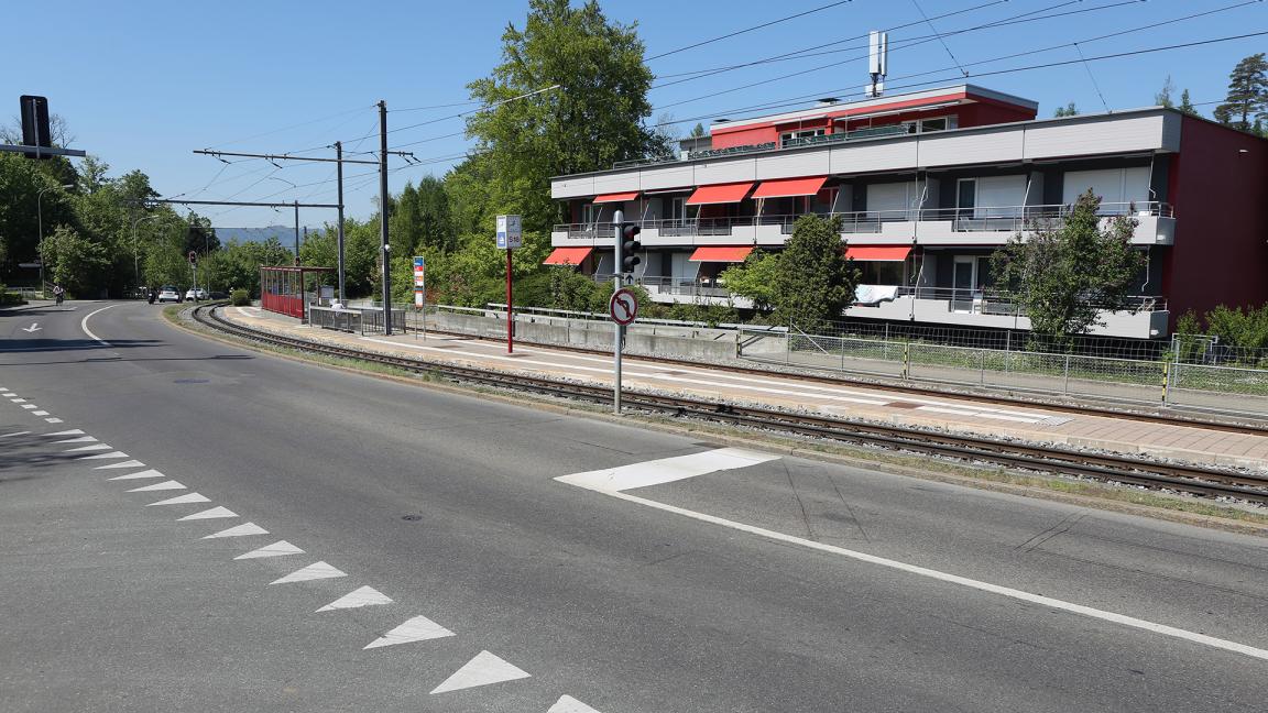 Strassenabschnitt mit Markierung für Kein Vortritt und Lichtsignal sowie Schienen und Mehrfamilienhaus im Hintergrund