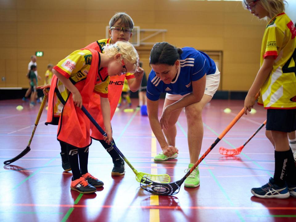 Eine Leiterin gibt einer Gruppe von Kindern Tipps im Unihockey Training