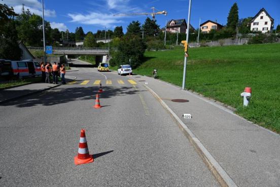 Strasse abfallend mit Trottoir rechts. Im Hintergrund Polizisten und verunfalltes Fahrrad