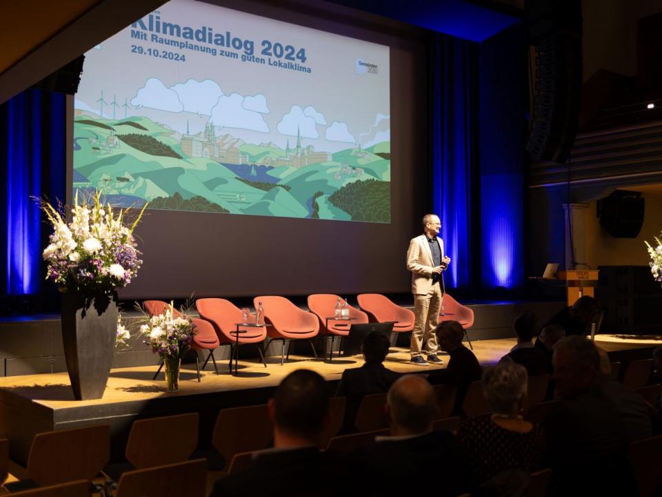 Martin Neukom auf der Bühne, im Hintergrund eine Illustration zum Klimadialog.