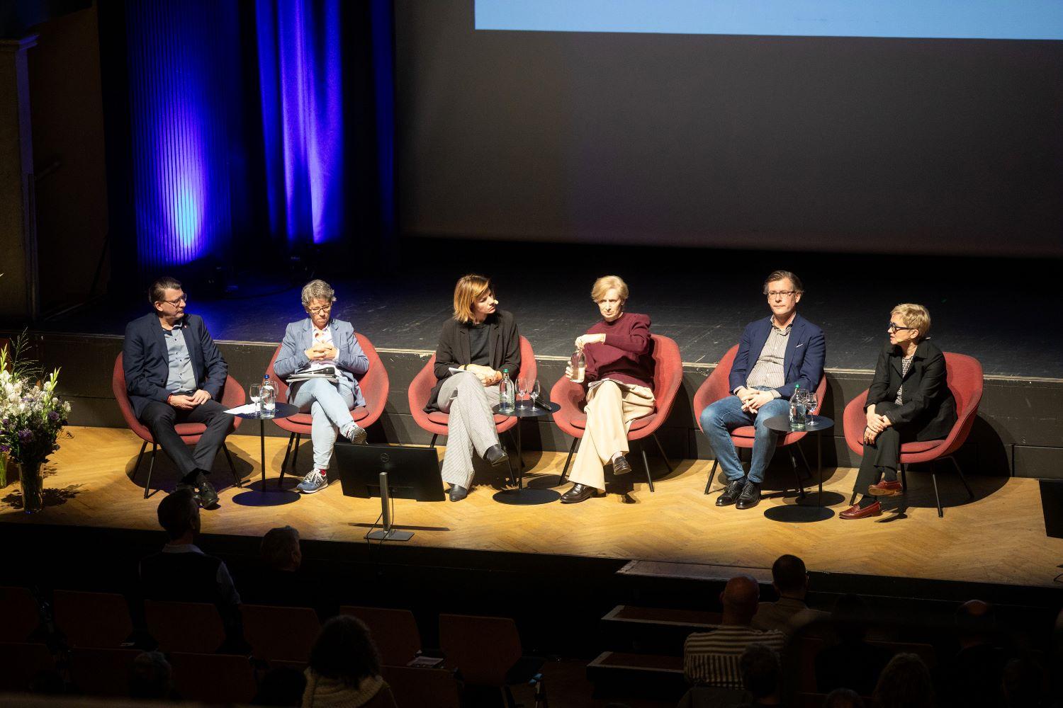 Die Podiumsgäste sitzen in einer Reihe auf der Bühne.