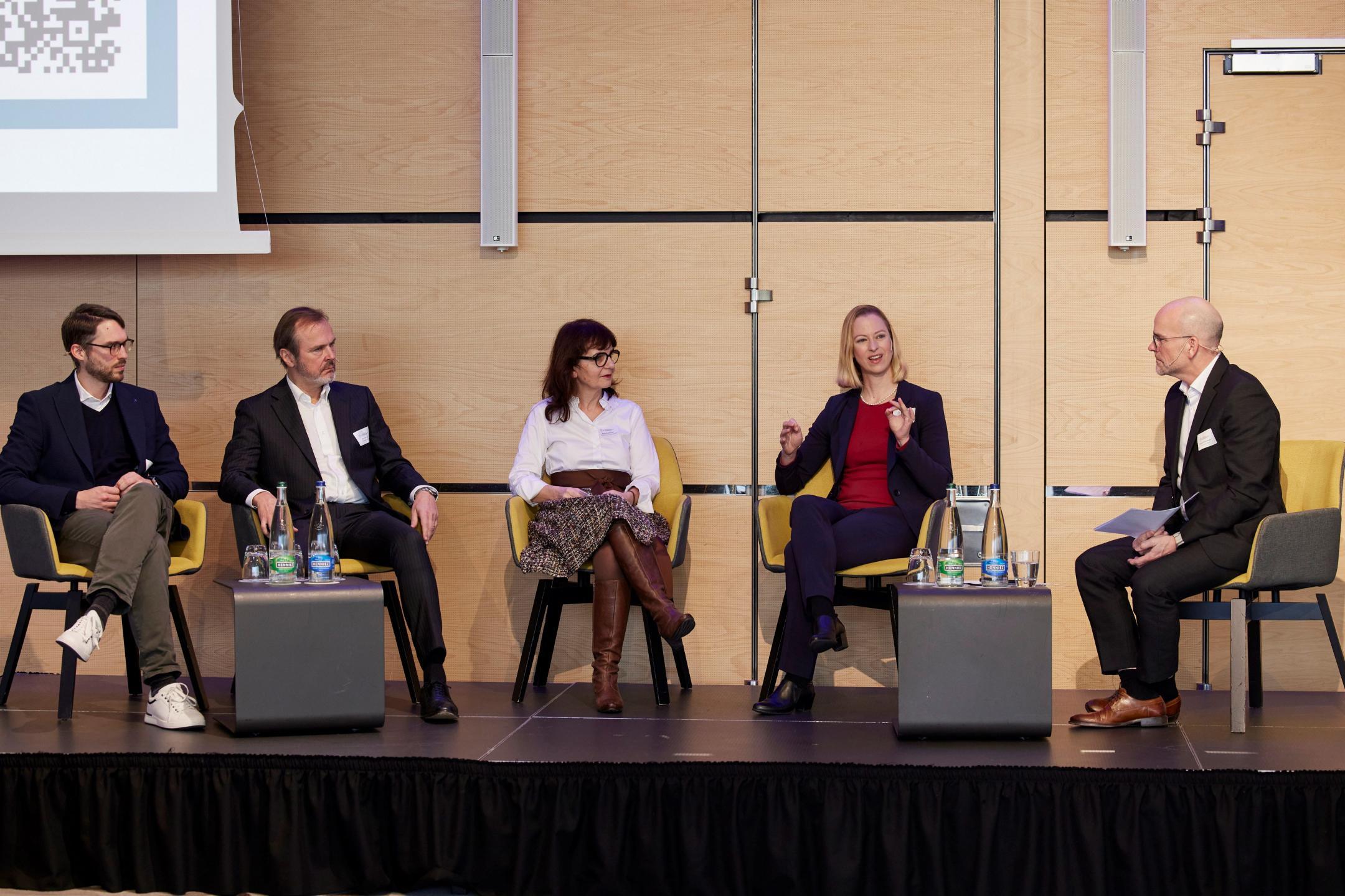 Zwei Männer und zwei Frauen sitzen zusammen mit einem Moderator auf einer Bühne und diskutieren miteinander.