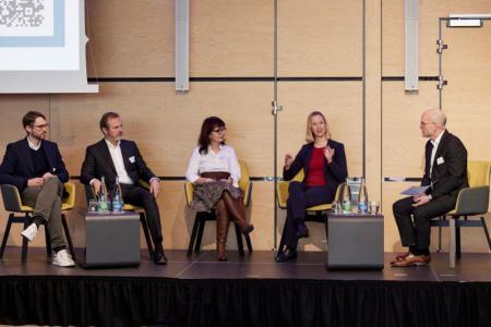 Zwei Männer und zwei Frauen sitzen zusammen mit einem Moderator auf einer Bühne und diskutieren miteinander.