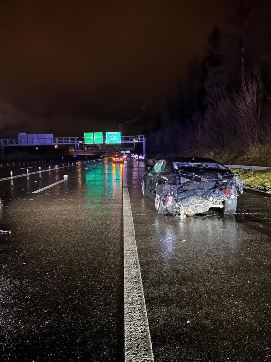 Unfallfahrzeug steht auf dem Pannenstreifen einer Autobahn bei Nacht und nasser Fahrbahn