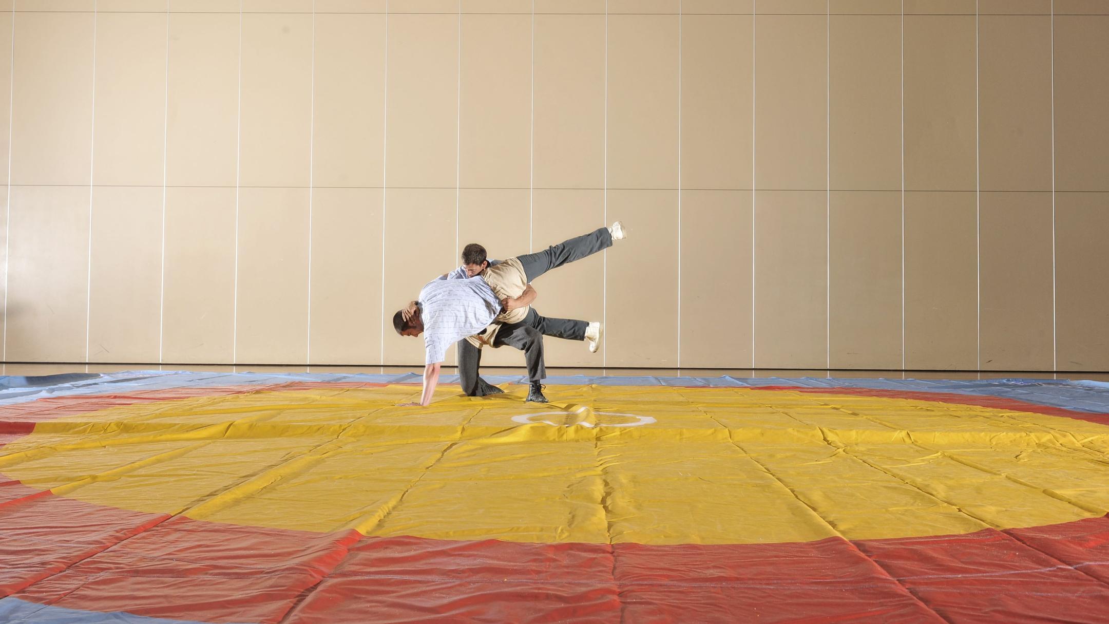 Zwei Männer in Schwingerhosen üben auf einer Indoor-Fläche ohne Sägemehl.