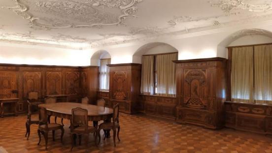 Raum mit Holzboden, Holzmöbeln und Stukkaturdecke.