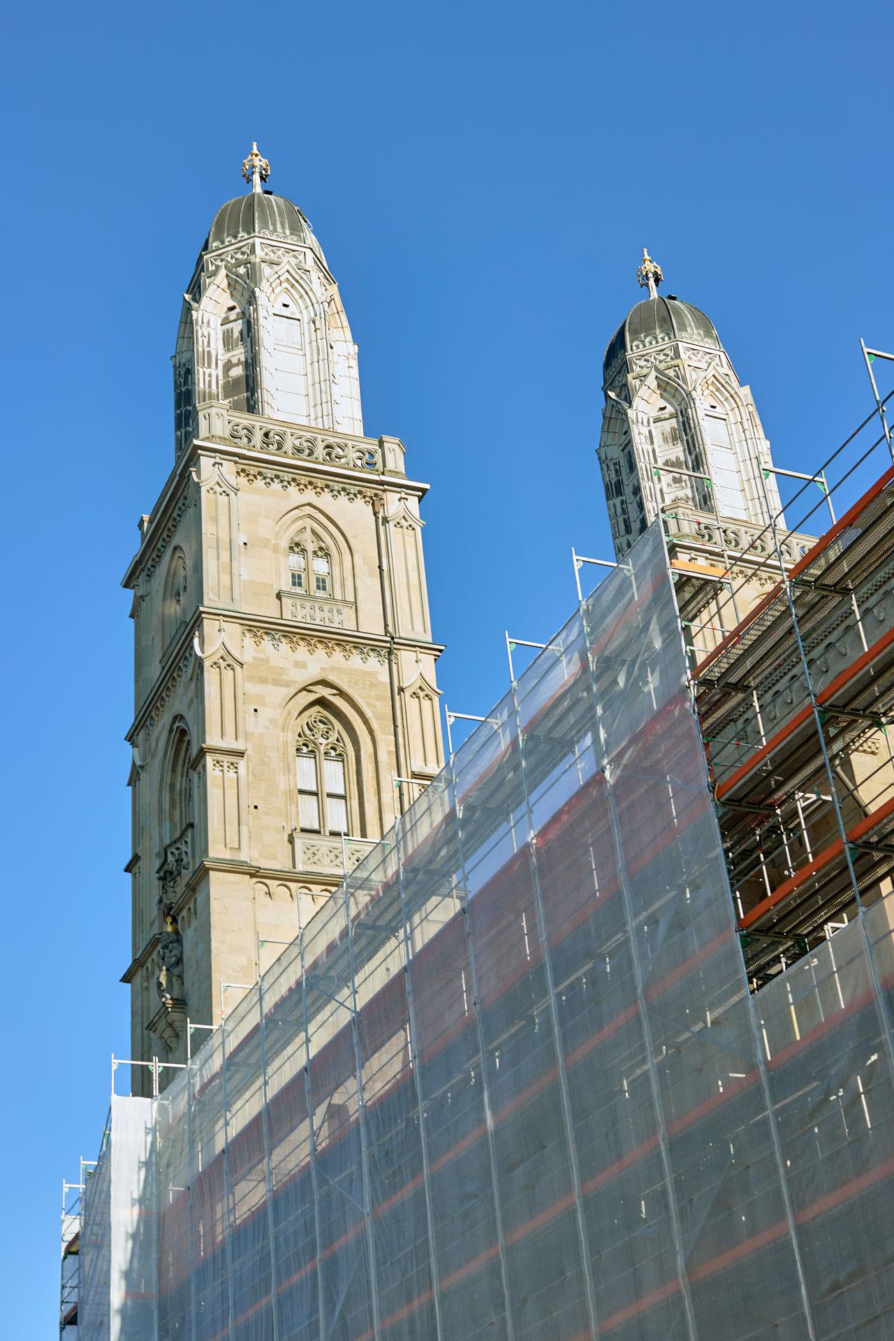 Zwei Türme des Grossmünsters in Zürich teilweise eingerüstet mit weissem Netz, unte