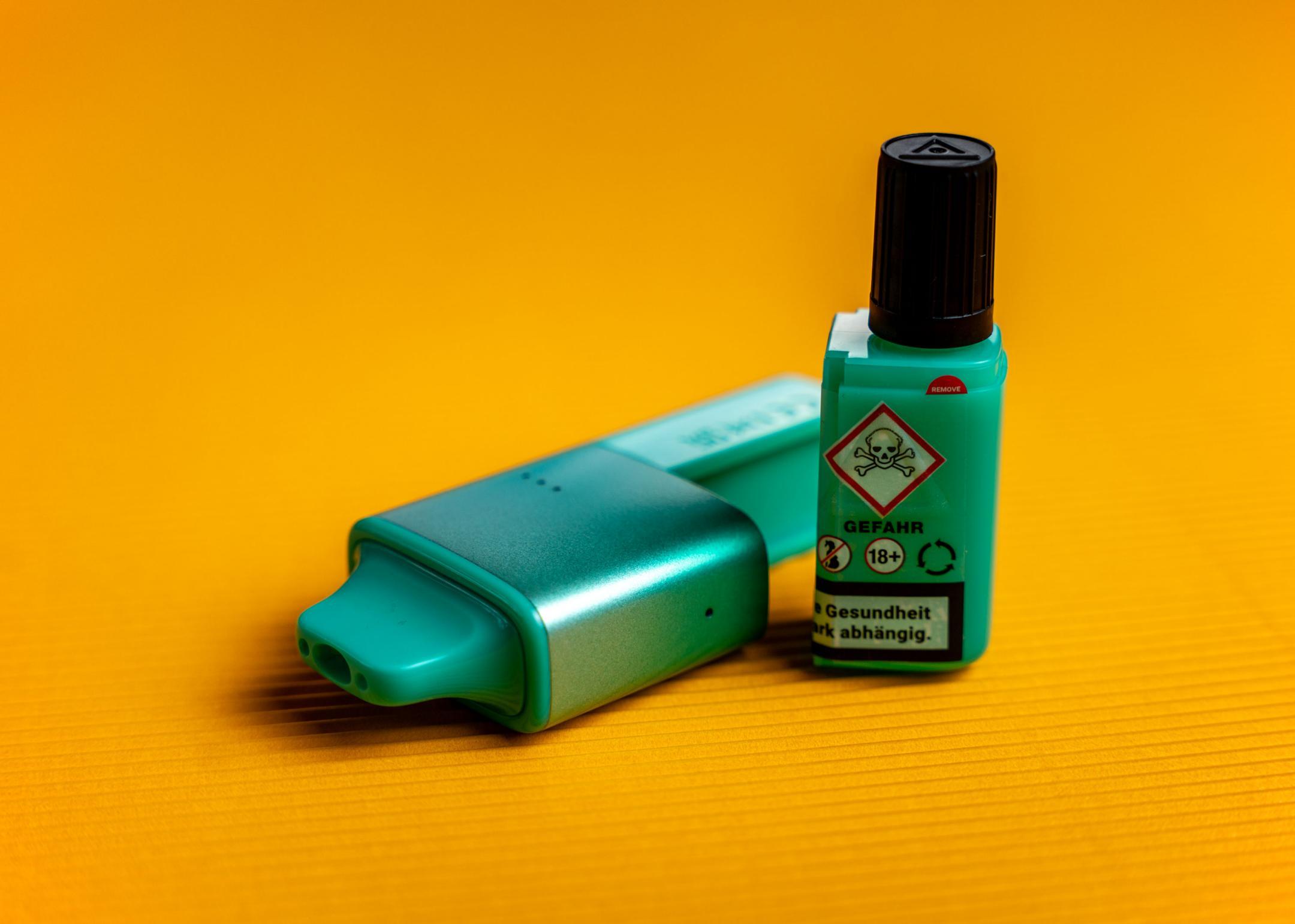 Türkiser Vape mit Nachfüllbehälter vor gelbem Hintergrund.