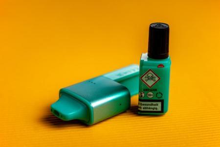 Türkiser Vape mit Nachfüllbehälter vor gelbem Hintergrund.