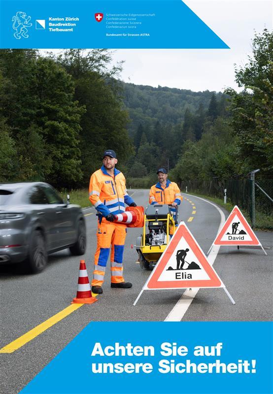 Zwei Strassenarbeiter in orangefarbener Arbeitskleidung sichern eine Fahrbahn mit Verkehrsleitkegeln und dreieckigen Warnschildern, die mit den Namen «Elia» und «David» beschriftet sind. Ein graues Auto fährt vorbei. Im Hintergrund Bäume und ein bewaldeter Hang. Der Text im Vordergrund lautet: «Achten Sie auf unsere Sicherheit!».