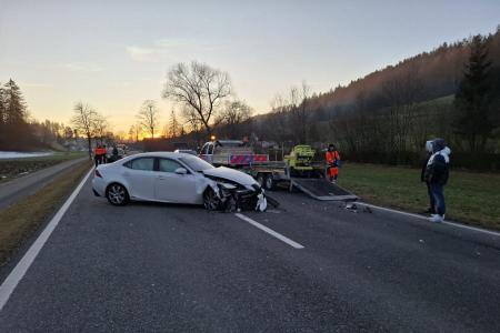 Ein weisser Personenwagen mit erheblichen Frontschäden steht nach einem Unfall quer auf einer Landstrasse. Ein Abschleppwagen ist vor Ort, und mehrere Personen, möglicherweise Einsatzkräfte, befinden sich in der Nähe.