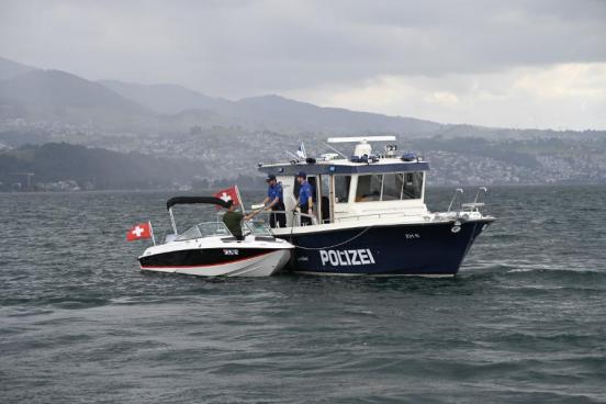 Ein Polizist auf einem Polizeiboot überreicht einem Mann auf einen kleineren Boot diverse Papiere.