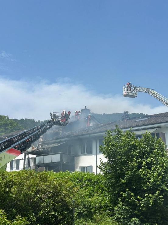 Aus einem Dach steig Rauch auf und Feuerwehrleute löschen von zwei Drehleitern aus.