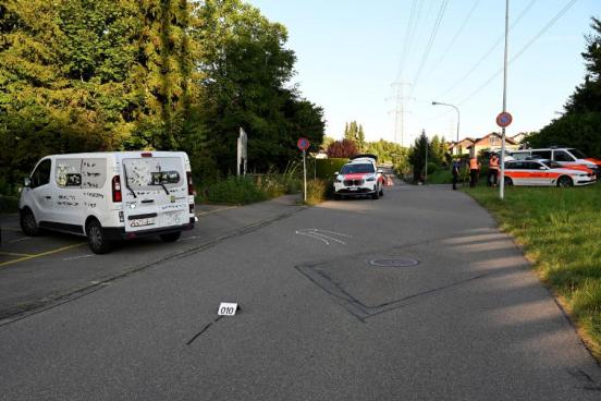 Eine Strasse und ein abgestellter Personenwagen; im Hintergrund die Polizei