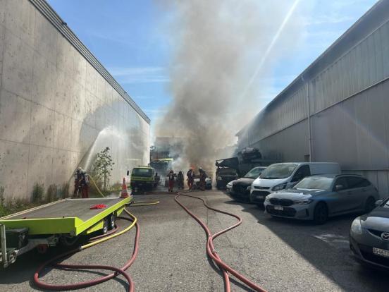 Die Feuerwehr löscht mehrere Fahrzeuge zwischen zwei Hallenwänden