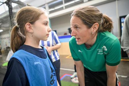 Eine Trainerin im grünen T-Shirt spricht zu einem Mädchen in einem blauen Trainingsüberzug.